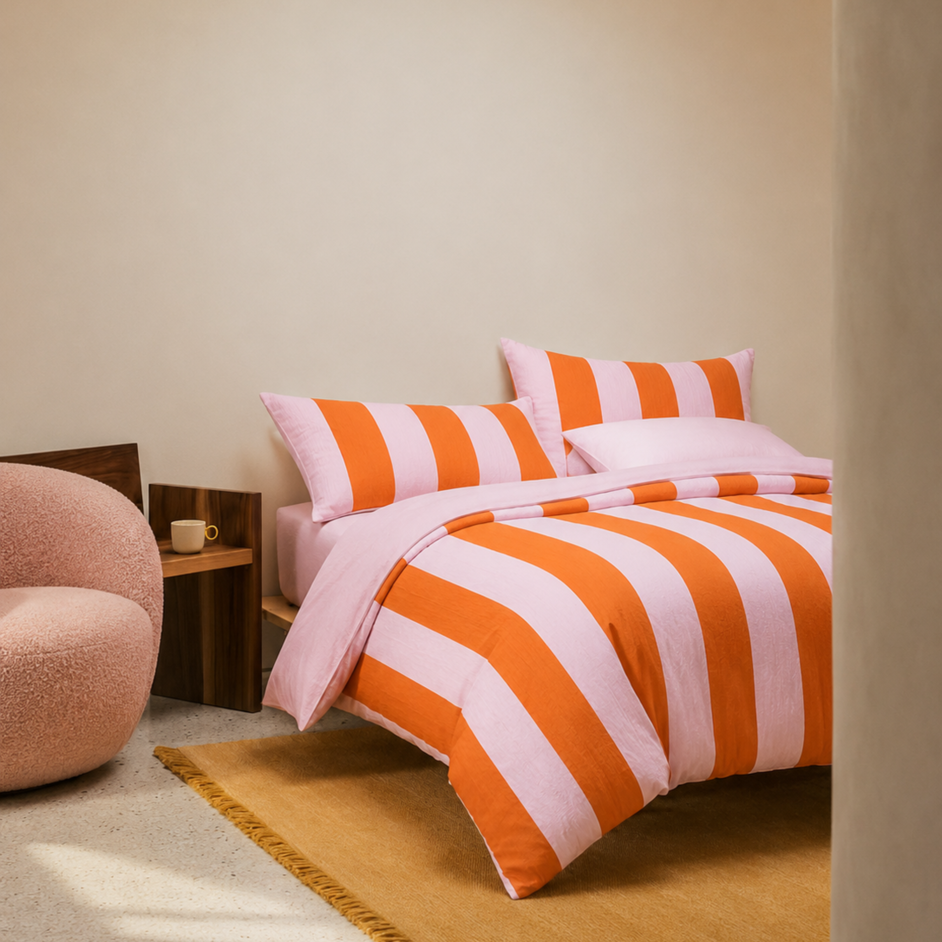 Ravello Stripe Bedding Set in bold pink and orange stripes, styled on a bed beside a mustard rug and boucle chair