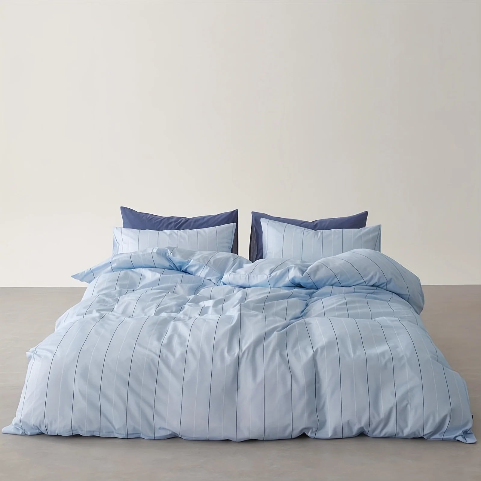 Aero Stripe Bedding Set in pale blue pinstripe cotton, styled with navy pillowcases on a made bed