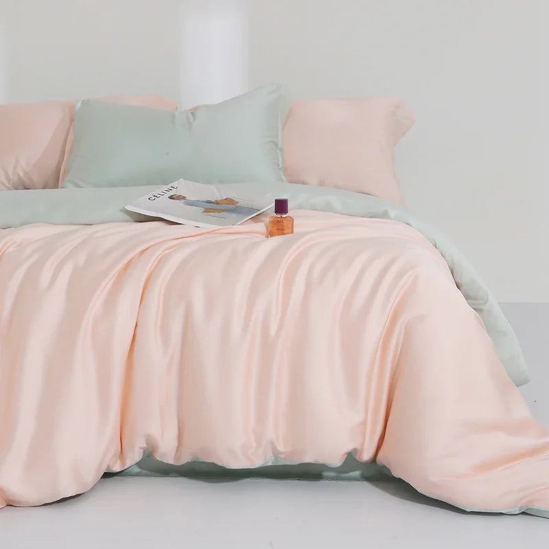Agnes Silk Bedding Set in Blush Pink with mint reverse, styled on a bed with a magazine and perfume bottle