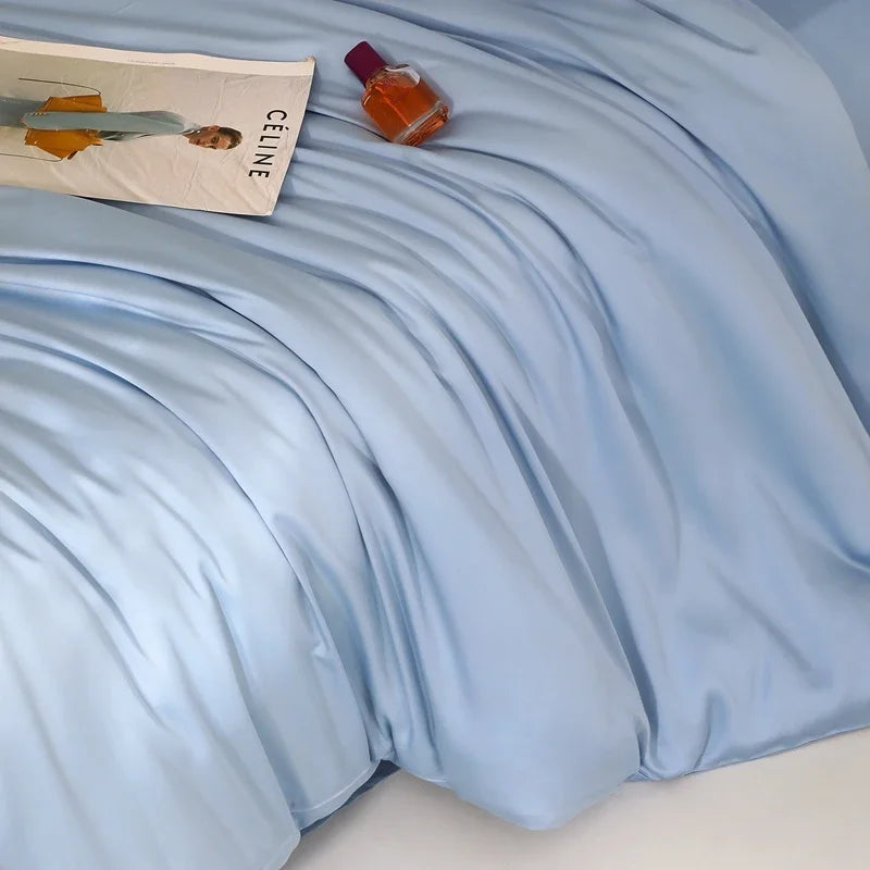 Close-up of pale blue Agnes Silk Bedding Set, soft sheen and draped folds, styled with magazine and perfume bottle