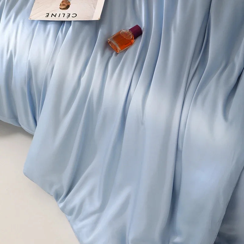 Close-up of the Agnes Silk Bedding Set in pale blue, silky draped folds with a perfume bottle resting on top