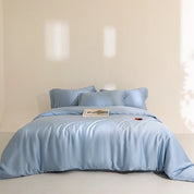 Agnes Silk Bedding Set in soft blue silk, styled on a made bed with a magazine and cherries