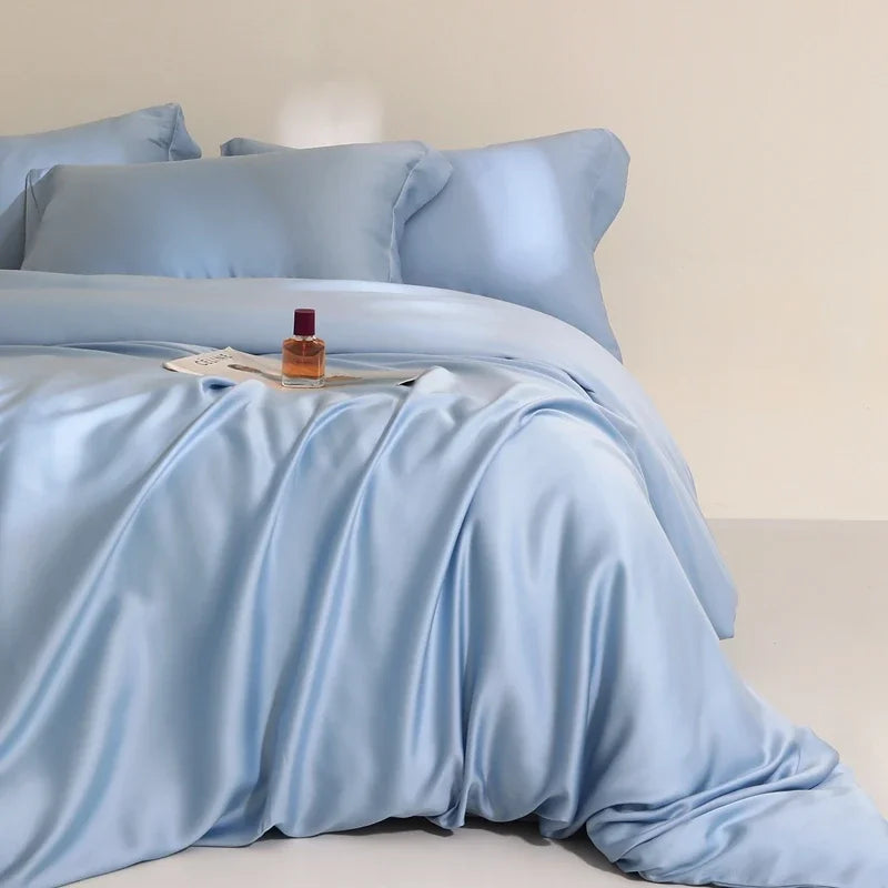 Agnes Silk Bedding Set in pale blue, draped in soft folds with a perfume bottle and magazine on top