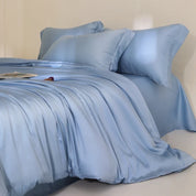 Agnes Silk Bedding Set in soft blue, draped in loose folds across a made bed with plump pillows