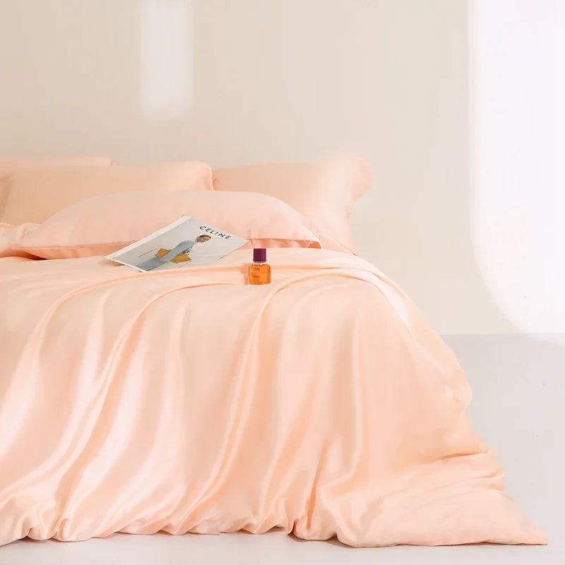 Agnes Silk Bedding Set in soft peach, made bed with silky sheen, styled with a magazine and perfume