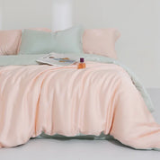 Agnes Silk Bedding Set styled on a bed in soft peach with mint green reverse, magazine and perfume bottle on top