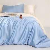 Agnes Silk Bedding Set in pale blue with cream reverse, softly draped on a bed with a magazine styled on top