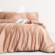 Agnes Silk Bedding Set in soft peach, draped in loose folds on a bed with a magazine styled on top