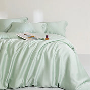 Agnes Silk Bedding Set in soft mint green, made bed with silky sheen, styled with a magazine and perfume