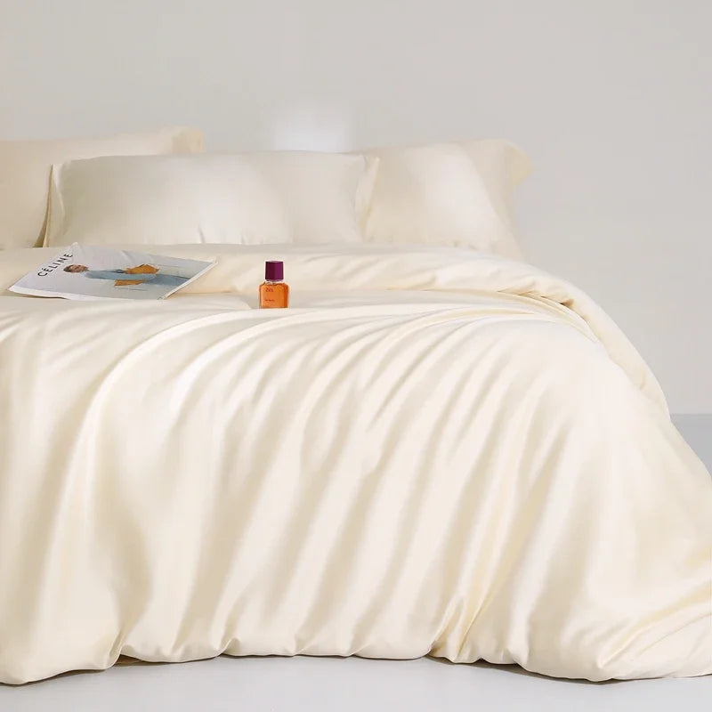 Agnes Silk Bedding Set in soft cream, draped on a bed with a magazine and perfume bottle styled on top
