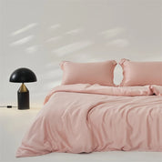 Amélie Bedding Set in Apricot Blush, soft pink lyocell silk on a made bed beside a black lamp