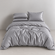 Amélie Bedding Set in Dove Grey, rumpled quilt cover with soft sheen and stacked pillowcases on a bed