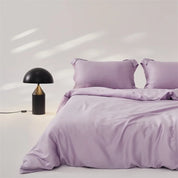Amélie Bedding Set in Lilac styled on a bed with soft sheen, beside a black dome table lamp
