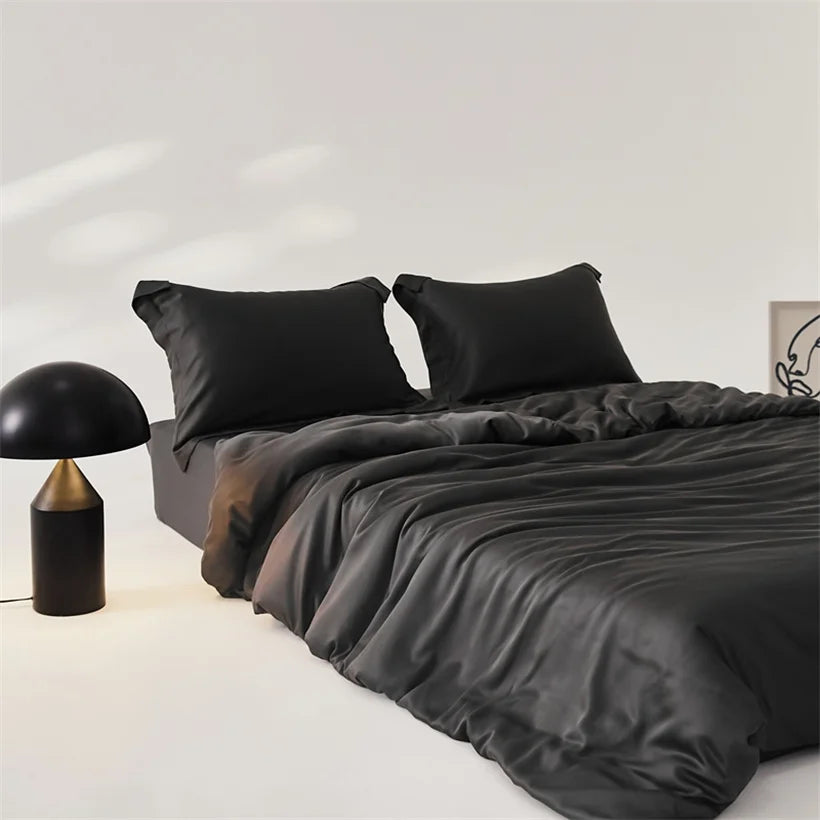 Amélie Bedding Set in Noir, deep black lyocell silk with soft sheen, styled on a bed beside a dome lamp
