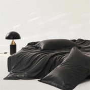 Amélie Bedding Set in Noir, draped in soft folds beside a dome table lamp, sheen catching the light