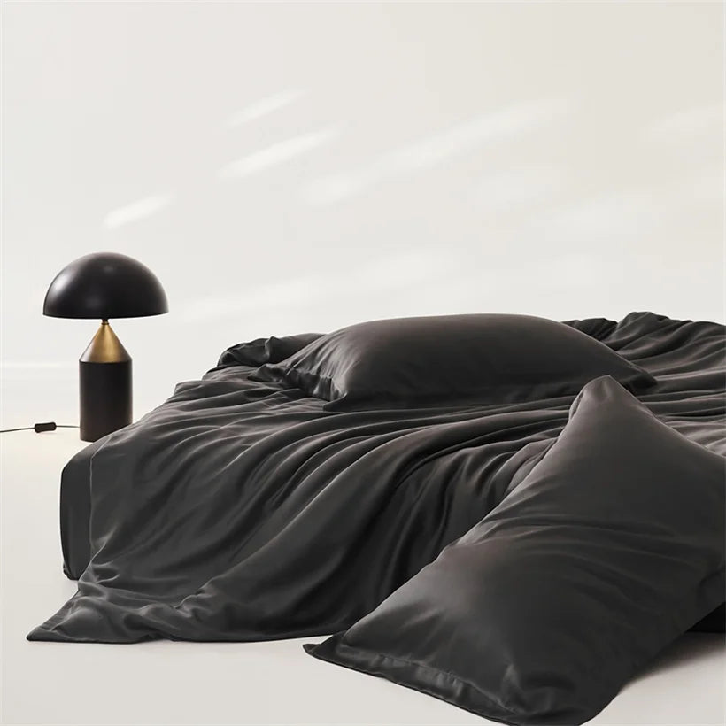 Amélie Bedding Set in Noir, draped in soft folds beside a dome table lamp, sheen catching the light