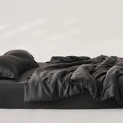 Amélie Bedding Set in Noir, rumpled black lyocell silk quilt cover and pillowcases on an unmade bed