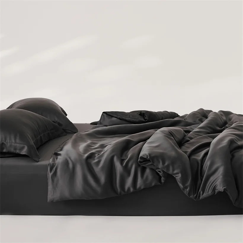Amélie Bedding Set in Noir, rumpled black lyocell silk quilt cover and pillowcases on an unmade bed