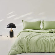 Amélie Bedding Set in Sage, sheeny green quilt cover and pillowcases on a made bed with black lamp