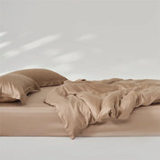 Amélie Bedding Set in Sandstone, rumpled quilt cover and pillowcases showing soft sheen on a bare mattress