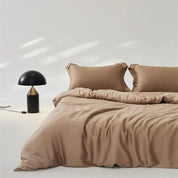 Amélie Bedding Set in Sandstone, soft lyocell silk quilt cover and pillowcases on a made bed beside a lamp