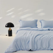 Amélie Bedding Set in pale sky blue, softly draped on a bed beside a black dome lamp