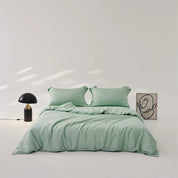 Amélie Bedding Set in soft sage green, styled on a bed with mushroom lamp and line-art print nearby