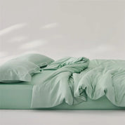 Amélie Bedding Set in soft sage green, quilt cover loosely rumpled atop fitted sheet and pillow