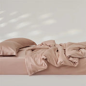 Amélie Bedding Set rumpled on a bed in dusty pink, lyocell silk catching soft light and sheen