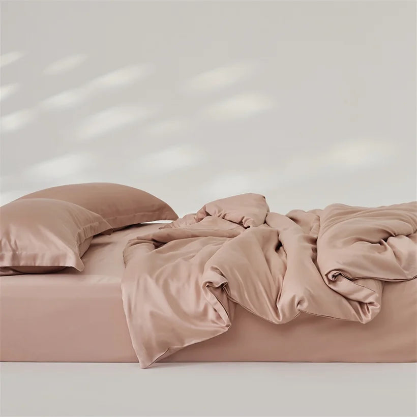 Amélie Bedding Set rumpled on a bed in dusty pink, lyocell silk catching soft light and sheen