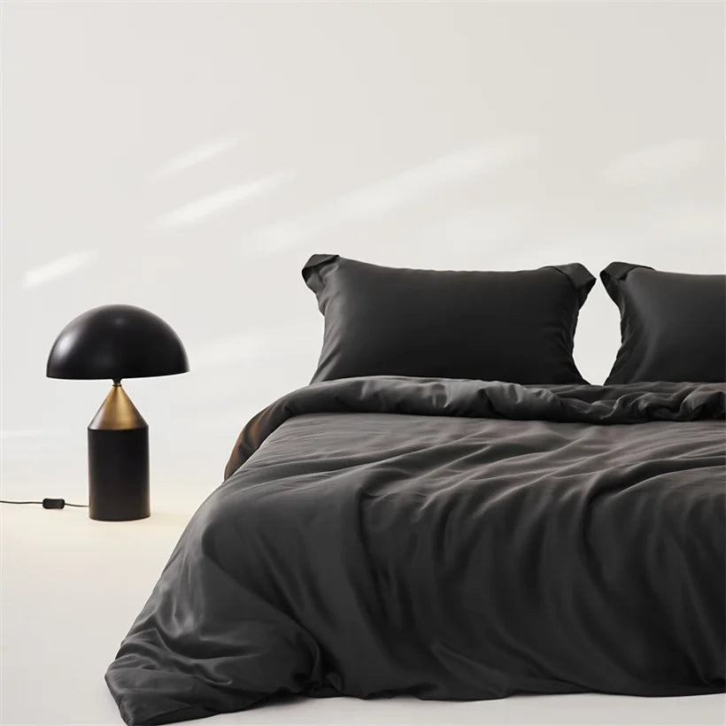 Amélie Bedding Set in charcoal black, made bed with sheen visible, styled beside a mushroom lamp