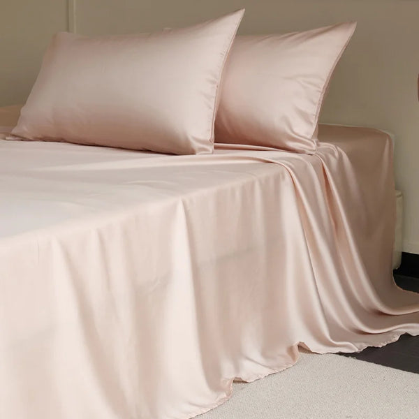 Amélie Flat Sheet Set in Blush Rose, draped over a bed with pillowcases showing soft satin sheen