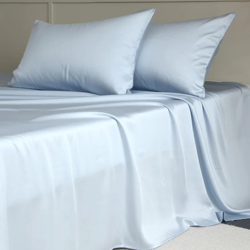 Amélie Flat Sheet Set in Celeste Blue, draped over a bed with two pillowcases showing a soft sheen