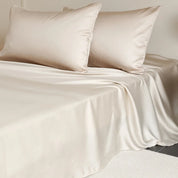 Amélie Flat Sheet Set in Champagne Gold, silky lyocell sheet and pillowcases draped over a made bed