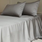 Amélie Flat Sheet Set in Dove Grey, draped over a bed with soft folds and lustrous sheen