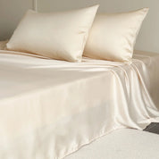 Amélie Flat Sheet Set in Golden Butter, draped over a made bed with soft lyocell silk sheen and pillowcases