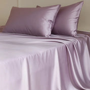 Amélie Flat Sheet Set in Lilac Bloom, lustrous lyocell silk draped over a made bed with pillows