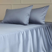 Amélie Flat Sheet Set in Sky Blue, silky lyocell draped over a made bed with two plump pillowcases