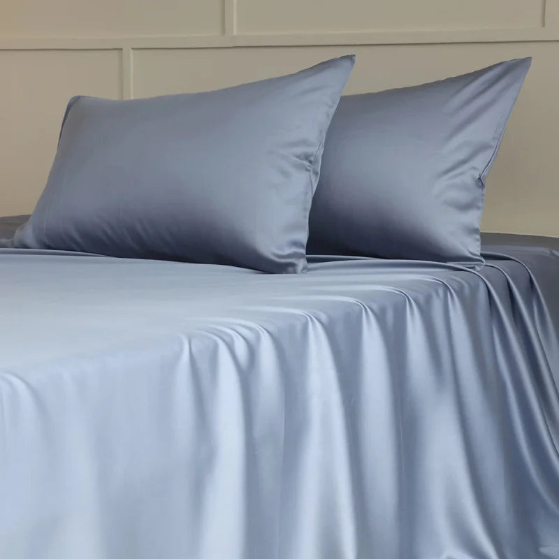 Amélie Flat Sheet Set in Sky Blue, silky lyocell draped over a made bed with two plump pillowcases