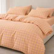 Avery Gingham Bedding Set in yellow and pink check, styled on a bed with solid peach pillowcases behind