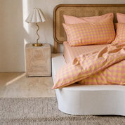 Avery Gingham Bedding Set in pink and yellow check styled on a bed beside a rattan headboard