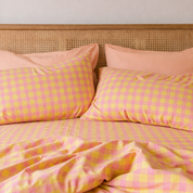 Avery Gingham Bedding Set in pink and yellow check, rumpled cotton against a rattan headboard
