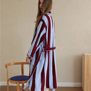 Side profile of the Bambi Striped Bath Robe in cherry red and pale blue stripes, worn belted over plush cotton