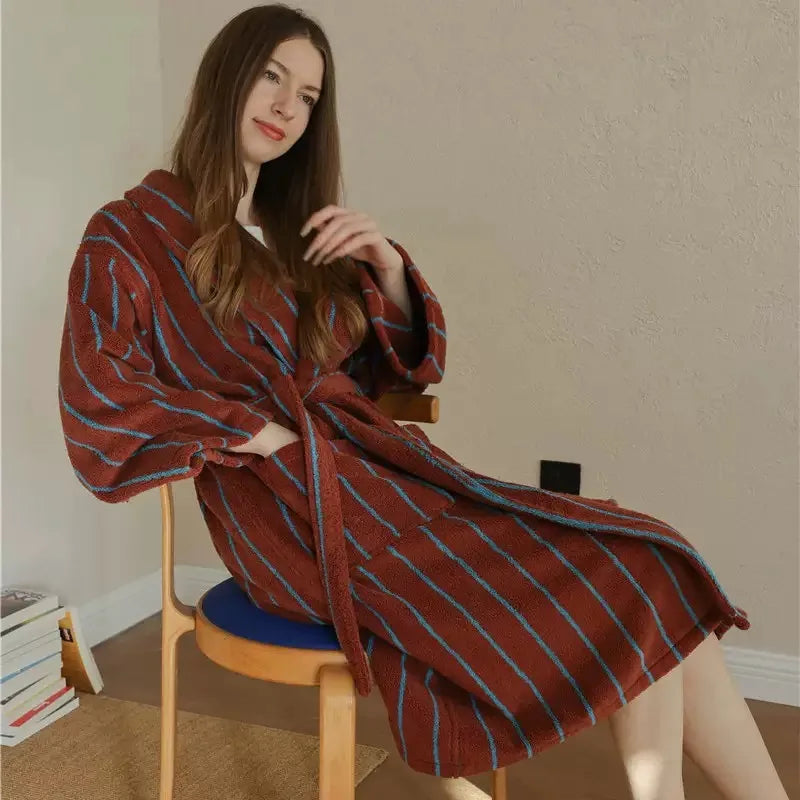 Woman seated on a stool wears the Bambi Striped Bath Robe in rust red with blue stripes, tied at the waist