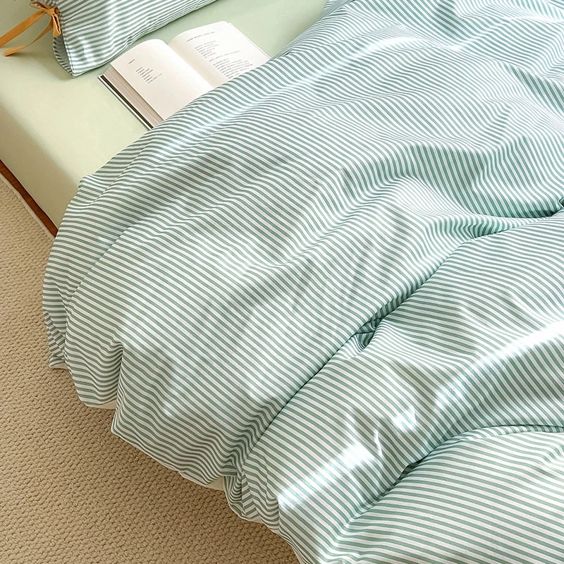 Close view of the Blossom Bow Bedding Set in Mint, fine green and white stripes draped over a bed with an open book