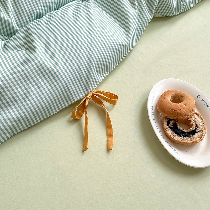 Close up of the mustard bow tie on the Blossom Bow Bedding Set in Mint, striped fabric beside a plate of bagels