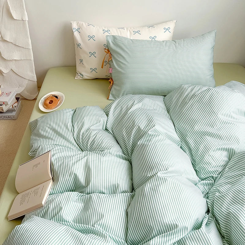 Blossom Bow Bedding Set in Mint, striped quilt cover rumpled on a bed with pillowcases and a book