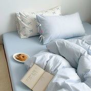 Blossom Bow Bedding Set in Sky, striped quilt cover and bow-print pillowcases styled with book and pastries