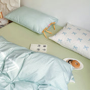 Blossom Bow Bedding Set styled on a bed, mint stripe pillowcase with bow ties beside a blue bow print case