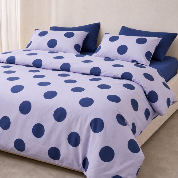 Della Spot Bedding Set styled on a bed, bold navy polka dots over a pale lilac blue cotton ground